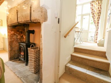A stone fireplace with a wood stove and wicker basket next to stairs leading to a room with a table and chairs at The Elbow in Frampton