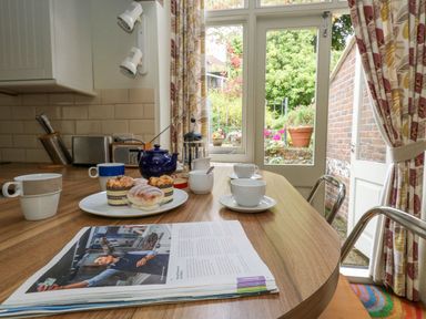 A kitchen table with cups, pastries, a teapot, a magazine, and a door opening to a garden at The Elbow in Frampton