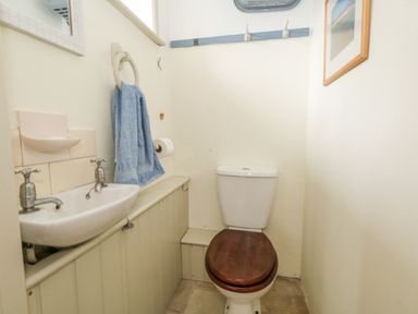 A small bathroom with a toilet with wooden seat and a sink with taps blue towel and toilet paper on wall at The Elbow in Frampton