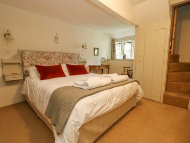 A bedroom with a bed with red pillows and folded towels a wooden desk and chair near a window at The Elbow in Frampton