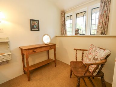 A small room with a wooden table with a round mirror and a wooden chair with a cushion and three windows with curtains at The Elbow in Frampton