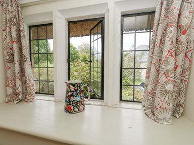 A window with three panes two curtains with floral pattern and a floral patterned jug on the windowsill at The Elbow in Frampton