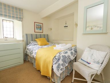A bedroom with a single bed with yellow bedding a chest of drawers a wicker chair and a wall mirror at The Elbow in Frampton