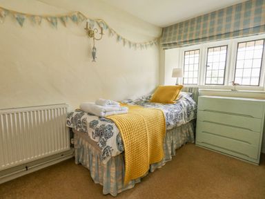 A bedroom with a single bed yellow quilt and cushions by a window with a chest of drawers and a radiator at The Elbow in Frampton