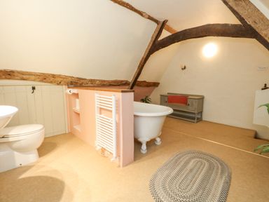 A bathroom with a toilet a clawfoot bathtub a gray bench and wooden ceiling beams at The Elbow in Frampton