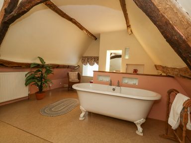 A bathroom with a freestanding bathtub wooden beams and a plant at The Elbow in Frampton