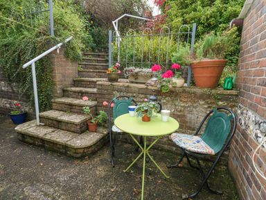 A small garden patio with a green round table and two chairs next to brick steps with potted plants at The Elbow in Frampton