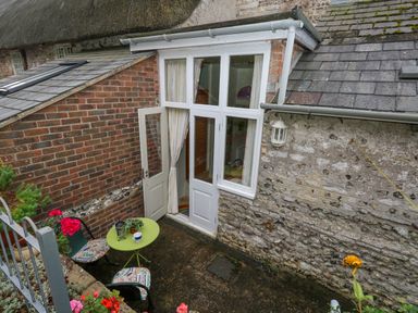 A small outdoor patio with a green round table and two chairs outside a white door at The Elbow in Frampton