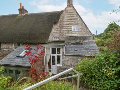A thatched roof cottage with a stone wall and garden in the foreground at The Elbow in Frampton