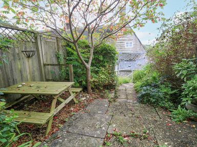 An outdoor garden area with a wooden picnic table tree and stone path leading to a house at The Elbow in Frampton