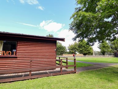 A wooden cabin with a deck and grass area at The Red in Llanerch Park near St Asaph