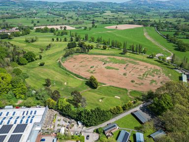 An aerial view of a golf course with sand traps and a dirt practice area surrounded by green fields