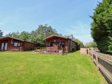 A log cabin with a lawn and fence at The Fallows in Llanerch Park near St Asaph