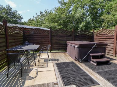 An outdoor area with a hot tub and a table with chairs at The Fallows in Llanerch Park near St Asaph