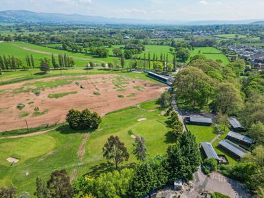 An aerial view of a golf practice range with grassy fields and trees at The Roe in Llanerch Park near St Asaph