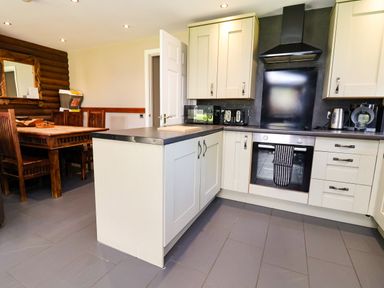 A kitchen with an island, oven, and wooden table at The Roe in Llanerch Park near St Asaph