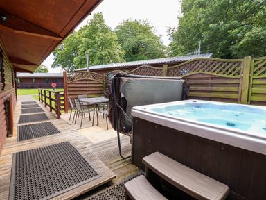 An outdoor patio with a hot tub and seating area at The Roe in Llanerch Park near St Asaph