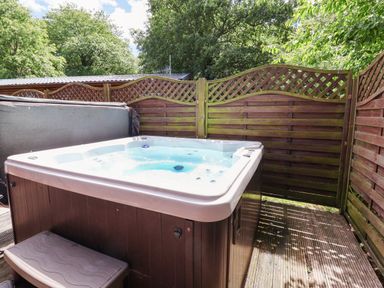 A hot tub on a deck surrounded by a privacy screen at The Roe in Llanerch Park near St Asaph