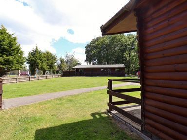 A log cabin with greenery and pathway at The Roe in Llanerch Park near St Asaph