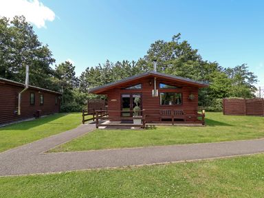 An outdoor view of a log cabin with a deck and greenery at The Roe in Llanerch Park near St Asaph