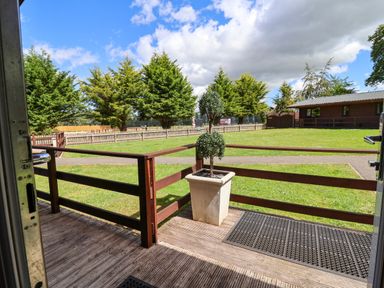 A view from a decking area showing trees and a fenced lawn at The Roe Llanerch Park near St Asaph