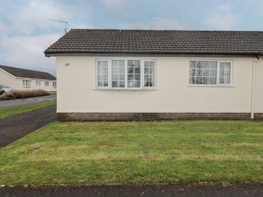 Exterior of a single-story house with tiled roof grass lawn and two sets of windows at 48 Gower Holiday Village in Scurlage