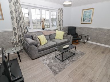 A living room with a gray sofa and yellow cushions a black chair a coffee table and a television at 48 Gower Holiday Village in Scurlage