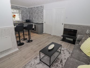A living room and kitchen area with a sofa and TV at 48 Gower Holiday Village in Scurlage