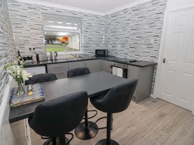 A kitchen with a countertop dining area with black chairs and grey cabinets at 48 Gower Holiday Village in Scurlage