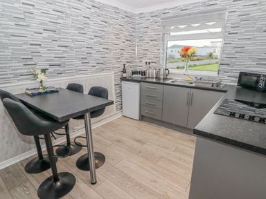 A kitchen with a black table and three chairs a countertop with appliances and a window with flowers at 48 Gower Holiday Village in Scurlage