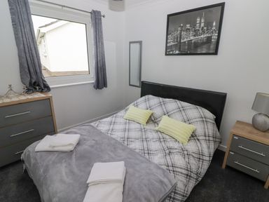 A bedroom with a double bed a framed cityscape photo bedside tables with lamps and folded towels on the bed at 48 Gower Holiday Village in Scurlage