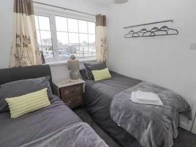 A bedroom with two single beds gray bedding a nightstand with lamp and window with curtains at 48 Gower Holiday Village in Scurlage