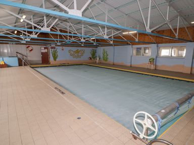 An indoor swimming pool covered with a pool cover inside a building with blue and beige walls and a mural of sea creatures at 48 Gower Holiday Village in Scurlage