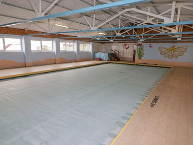 An indoor swimming pool covered with a pool cover with metal beams and murals of seaweed and an octopus on the walls at 48 Gower Holiday Village in Scurlage