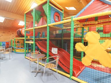 An indoor children's play area with slides climbing structures and tables with chairs at 48 Gower Holiday Village in Scurlage