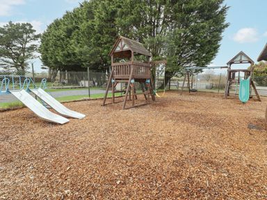 An outdoor playground with slides swings and climbing structures surrounded by wood chips at 48 Gower Holiday Village in Scurlage