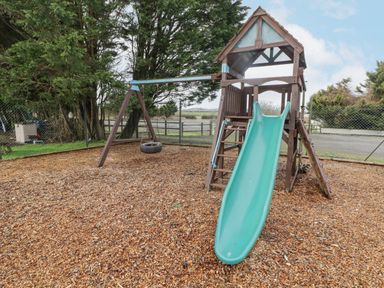 A children's playground with a slide swing and climbing structure outdoors at 48 Gower Holiday Village in Scurlage