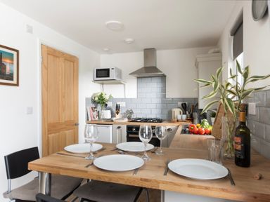 A kitchen with a wooden dining table set for four near a stove and a microwave at Bushwood Lodge in Wendron near Helston