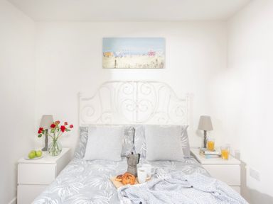 A bedroom with a white metal bed frame two nightstands with lamps and drinks at Bushwood Lodge Wendron near Helston