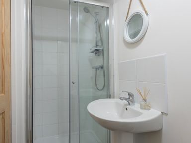A bathroom with a glass shower enclosure a white sink with a faucet and a round mirror hanging on the wall at Bushwood Lodge in Wendron near Helston