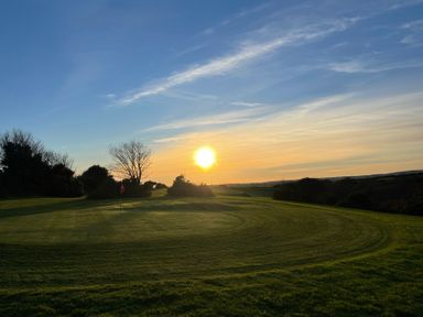 A golf course green with a hole and flag at sunset surrounded by trees and bushes at Bushwood Lodge in Wendron near Helston
