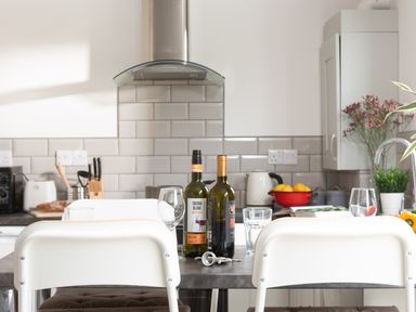 A kitchen with white chairs a table with wine bottles glasses and keys and a tiled backsplash at Wheal Jewel Lodge Wendron near Helston