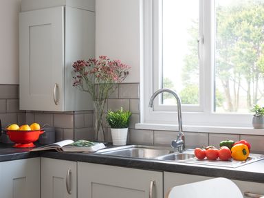 A kitchen counter with a sink and faucet near a window with vegetables flowers and a bowl of lemons at Wheal Jewel Lodge in Wendron near Helston