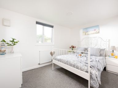 A bedroom with a white metal bed frame bedside tables a window and a white dresser at Wheal Jewel Lodge Wendron near Helston