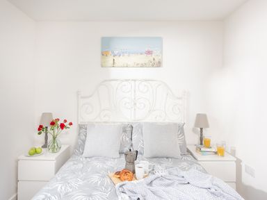 A bedroom with a white metal bed frame two bedside tables with lamps and books and flowers on one table at Wheal Jewel Lodge in Wendron near Helston