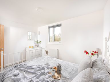 A bedroom with a bed, bedside lamp, dresser, mirror, window, and breakfast tray at Wheal Jewel Lodge in Wendron near Helston