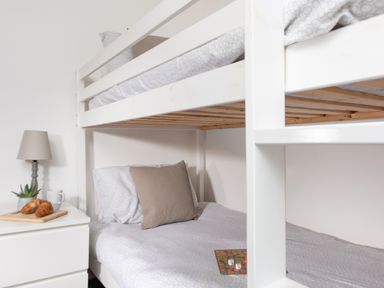 A bunk bed with pillows and bedding next to a nightstand with a lamp croissants and a plant at Wheal Jewel Lodge Wendron near Helston