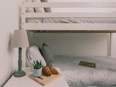 A bunk bed with pillows and a board game on the bottom bed and a bedside table with a lamp plant and croissants at Wheal Jewel Lodge Wendron near Helston