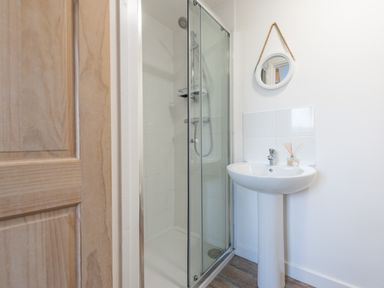 A bathroom with a glass door shower enclosure a round mirror hanging on the wall and a pedestal sink at Wheal Jewel Lodge Wendron near Helston
