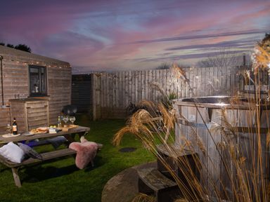 An outdoor area with a wooden picnic table set with food and drinks a wooden hot tub and a fence at Wheal Jewel Lodge in Wendron near Helston